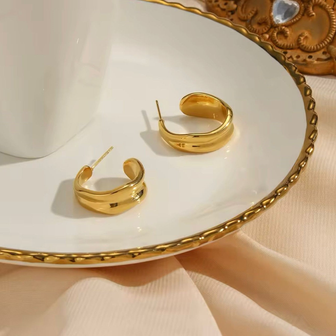 A pair of 18K gold plated stainless steel loop hoop earrings displayed on a plate.