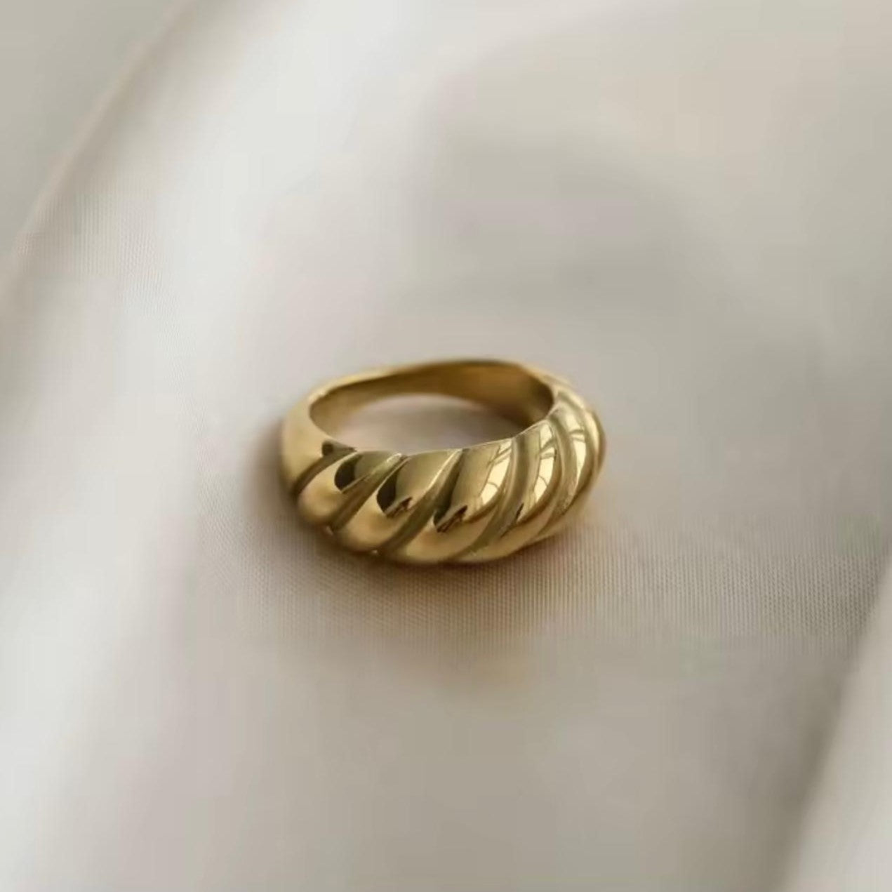 A gold-plated stainless steel ring with a curved design, displayed on a white surface.