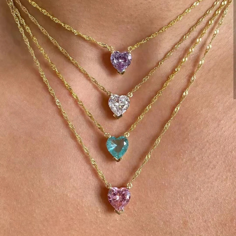A collection of heart-shaped necklaces in gold color with different colored gemstones displayed on neck.