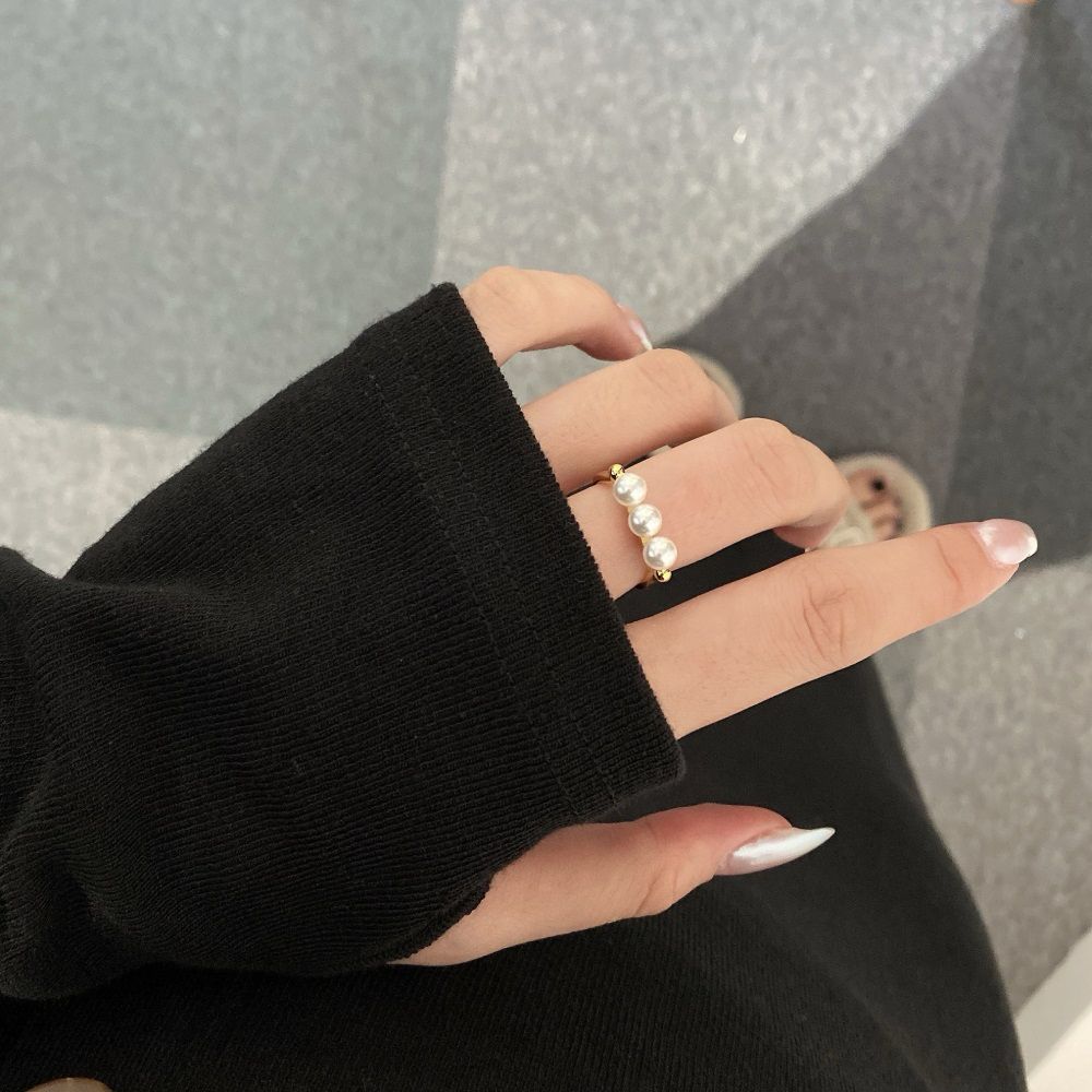 An adjustable ring with 925 sterling silver band and gold plating, featuring three white shell pearls aligned in a row.
