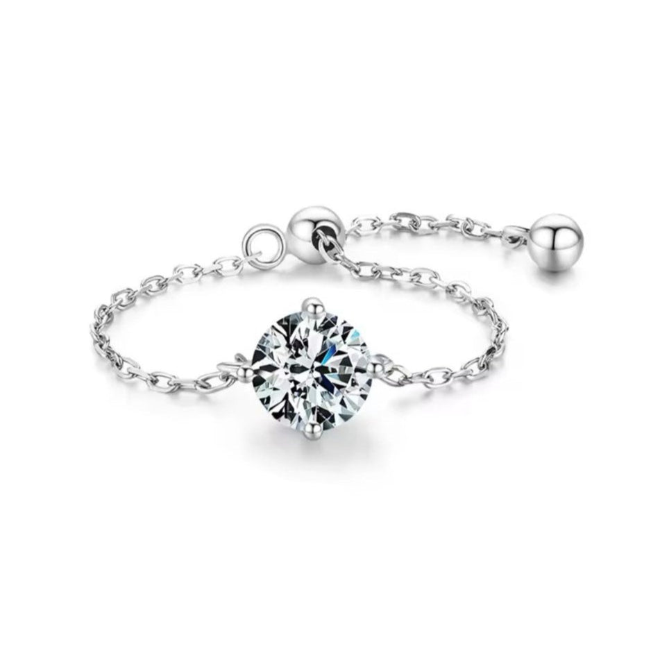 An adjustable sterling silver ring with a gold/silver color, featuring a single clear cubic zirconia stone, linked to a chain of gold-tone beads.