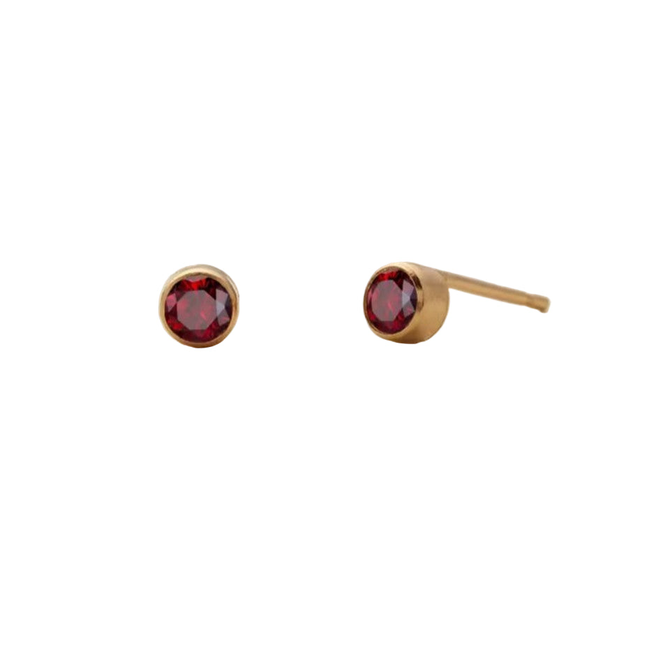 Gold stud earrings with red gemstones on a beige background