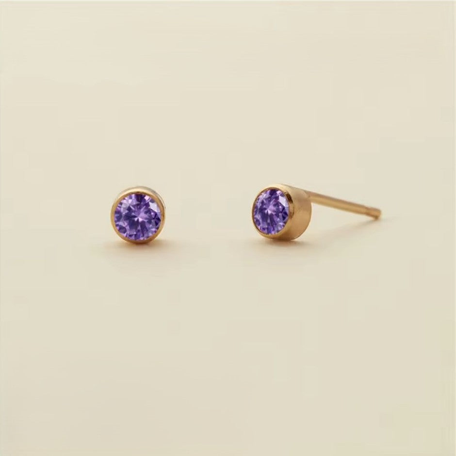 Gold stud earrings with purple gemstones on a beige background