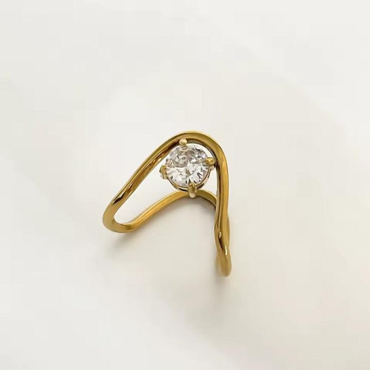 A circular teardrop gold ring with clear gemstone on a white background