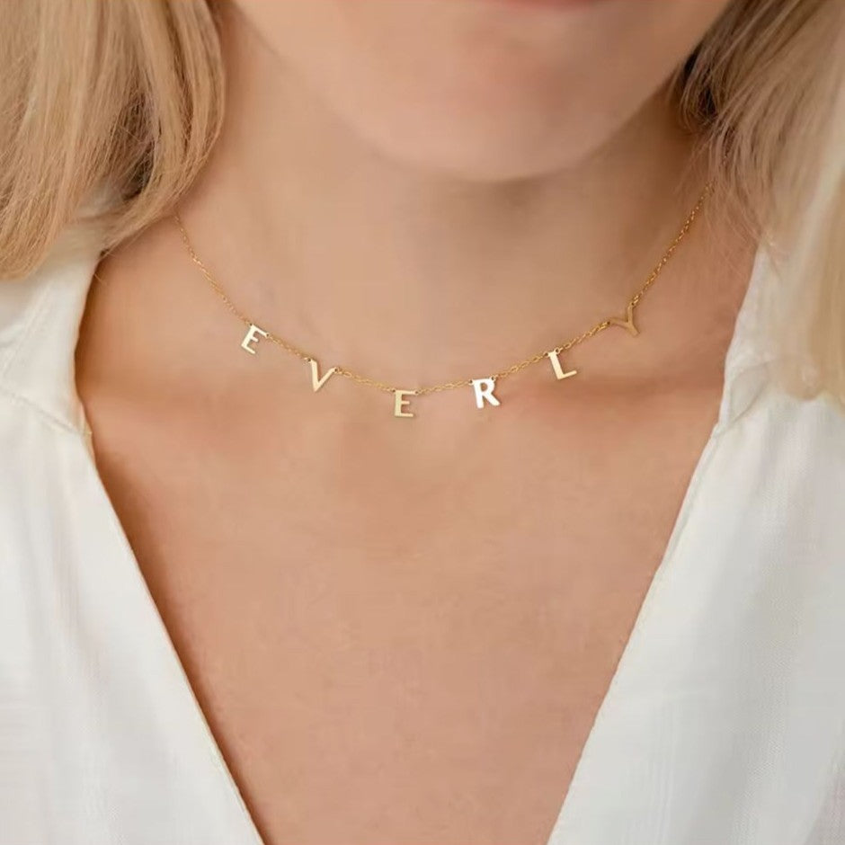 Gold necklace with 'EVERLY' letters worn by a person in a white top