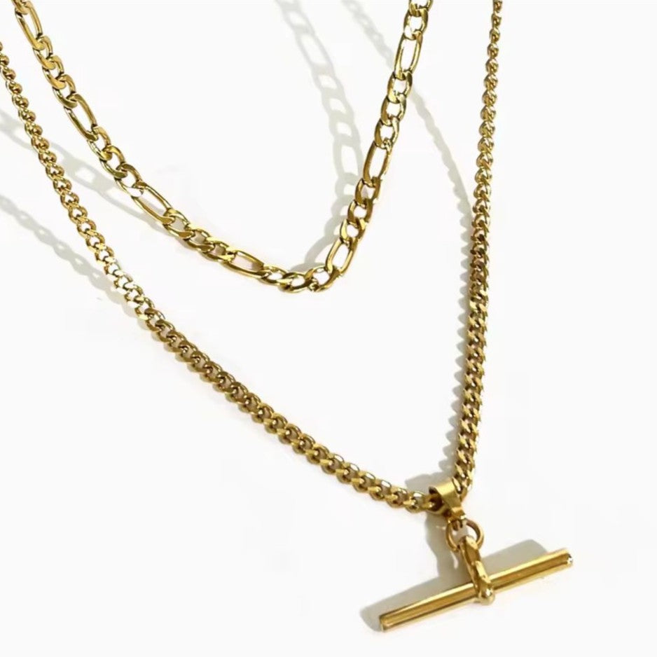 Gold chain necklace with a T bar pendant on a white background