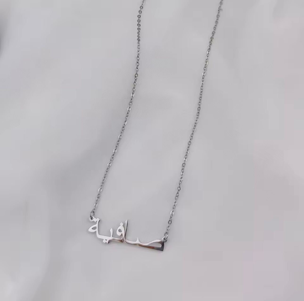Silver necklace with Arabic name on a light gray background