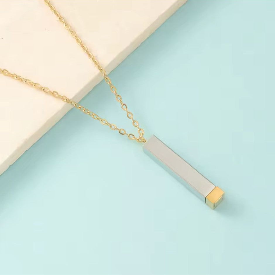 Gold necklace with a rectangular pendant on a light blue background