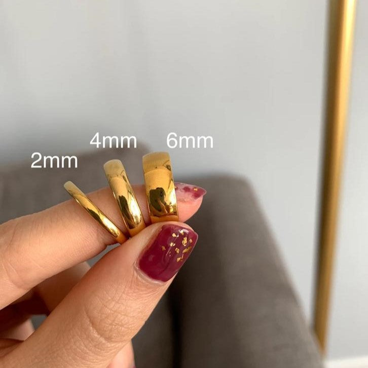 A hand holding three gold-colored knuckle rings of different sizes: 2mm, 4mm, and 6mm.