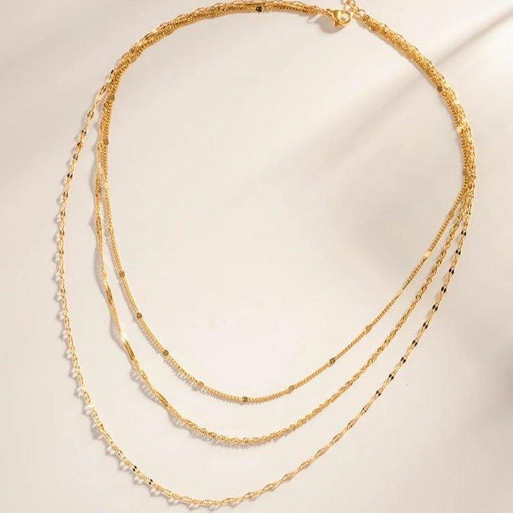 A gold-colored, layered chain necklace with three rows of stainless steel links.