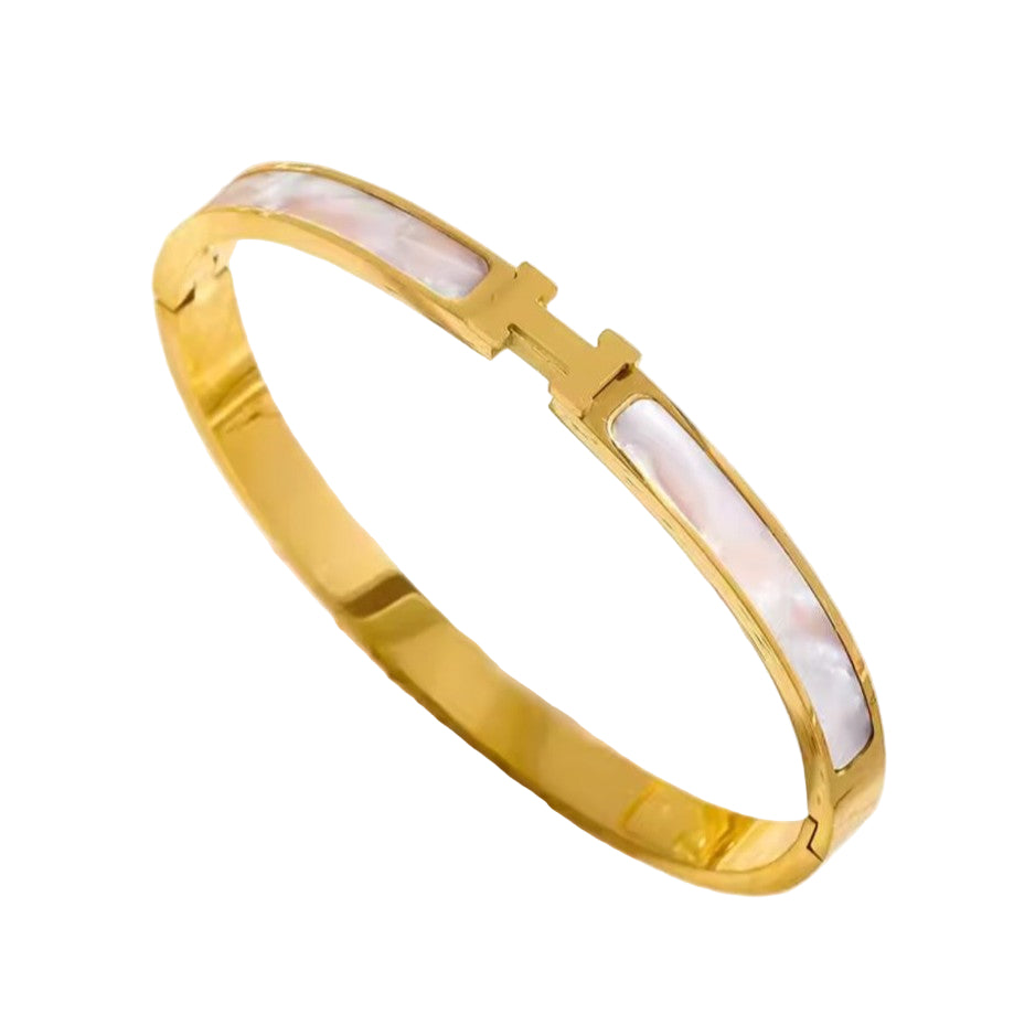 Gold H bracelet with a opal stone on a beige background