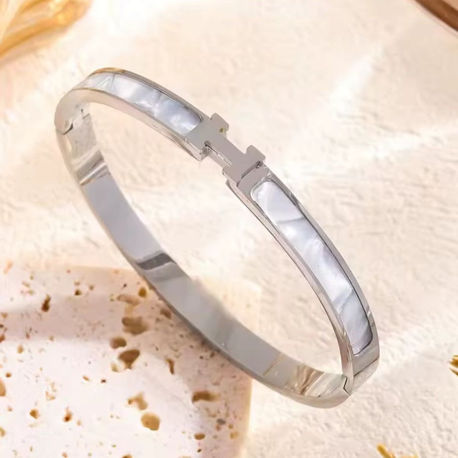 Silver H bracelet with a opal stone on a textured beige background