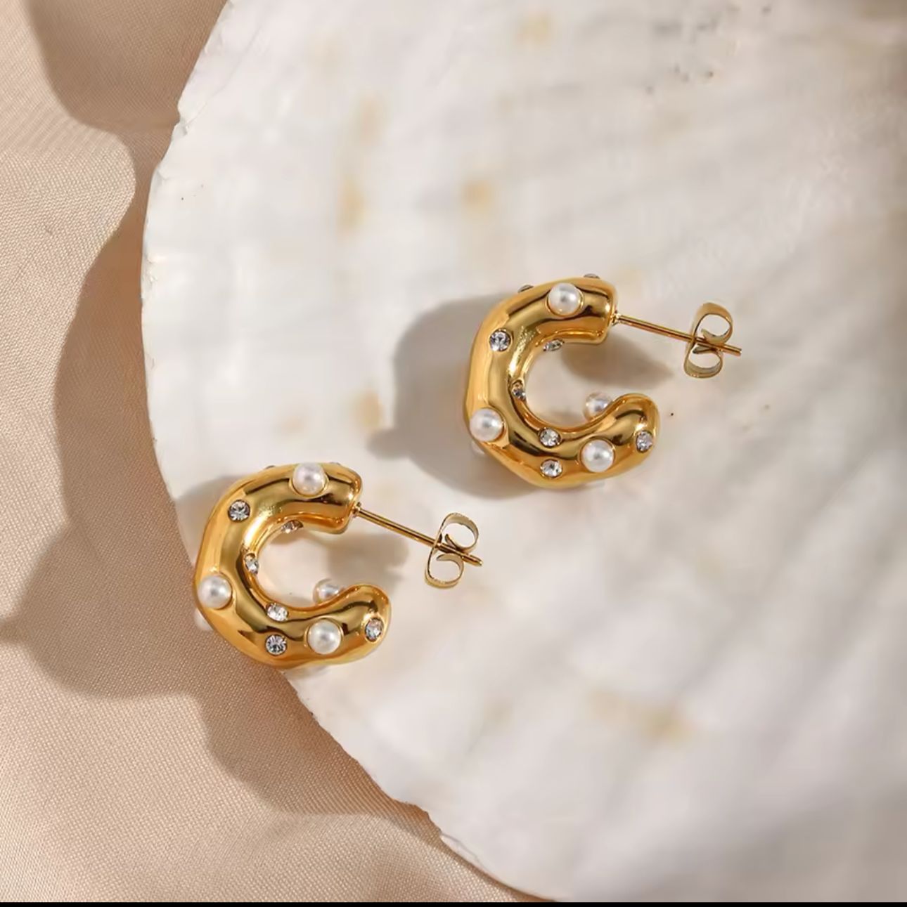 A pair of 18k gold-plated stainless steel hoop earrings with curved design and embellished with pearls and shimmering accents.