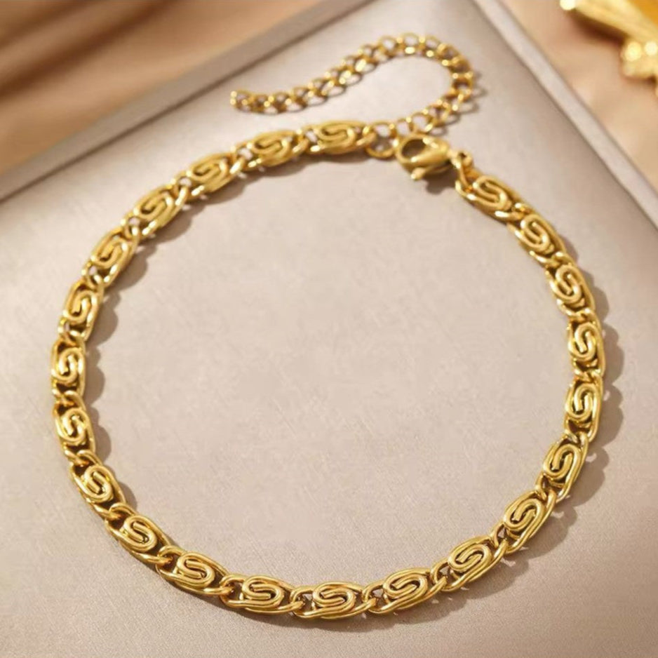 A gold-colored stainless steel bracelet with a geometric pattern, displayed on a neutral background.