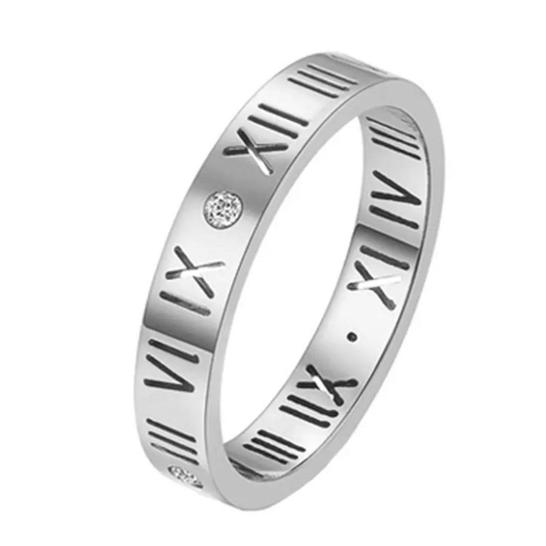 A silver-colored stainless steel band ring with Roman numeral patterns and small embellishments.