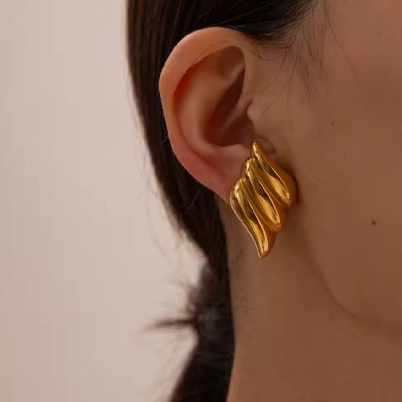 Gold earring worn on an ear with a neutral background