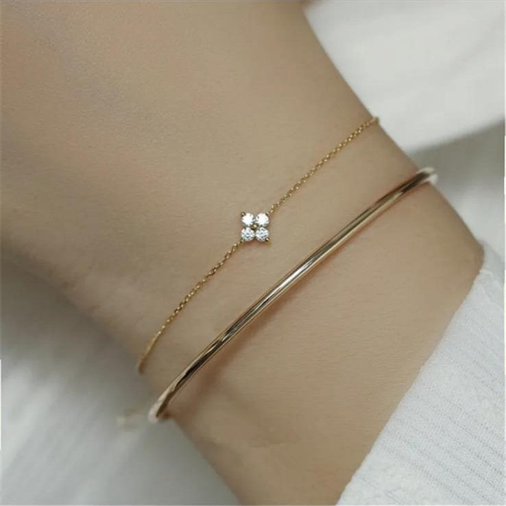 A close-up image of a person's wrist wearing a small dainty bracelet with a single flower design. The bracelet is made of 925 sterling silver and appears in a gold tone.