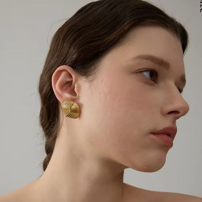 A 14k gold plated stainless steel geometric earring with a ribbed texture displayed on a women's ear.