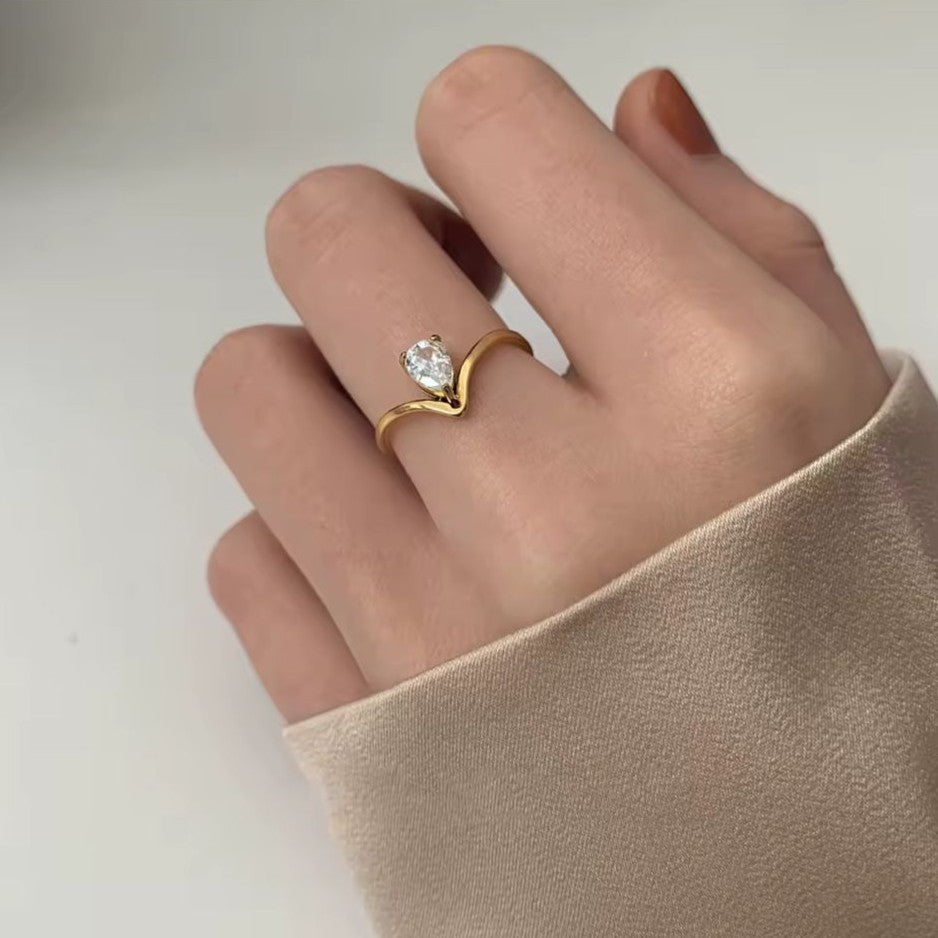 V-shaped stainless steel gold ring with a diamond on a hand against a plain background