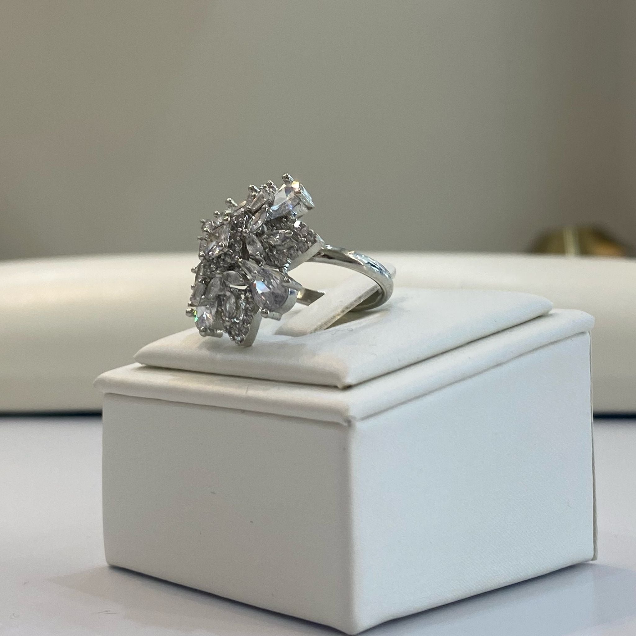 An elegant silver adjustable gemstone ring with a prominent clear white center stone and intricate detailing, displayed on a white box.