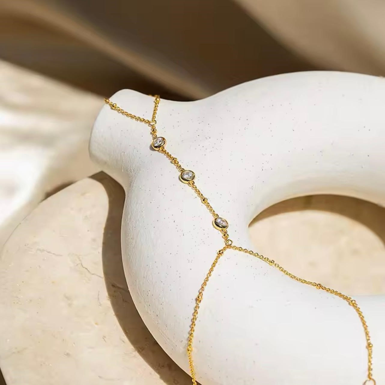A delicate gold chain bracelet with bezel-set crystal accents, displayed on a white sculpture.