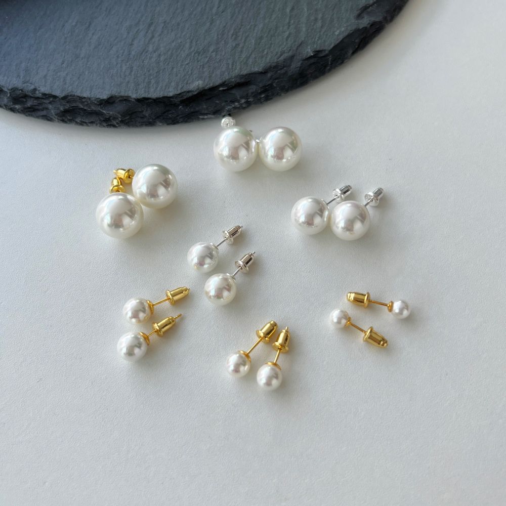 Pairs of classic pearl stud earrings with lustrous pearls set against a off-white backing.
