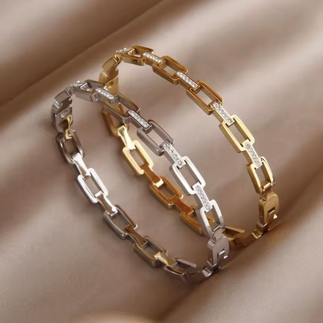 Two stainless steel hollow geometric bangles, one with a gold finish and the other with a silver finish, displayed on a textured fabric surface.