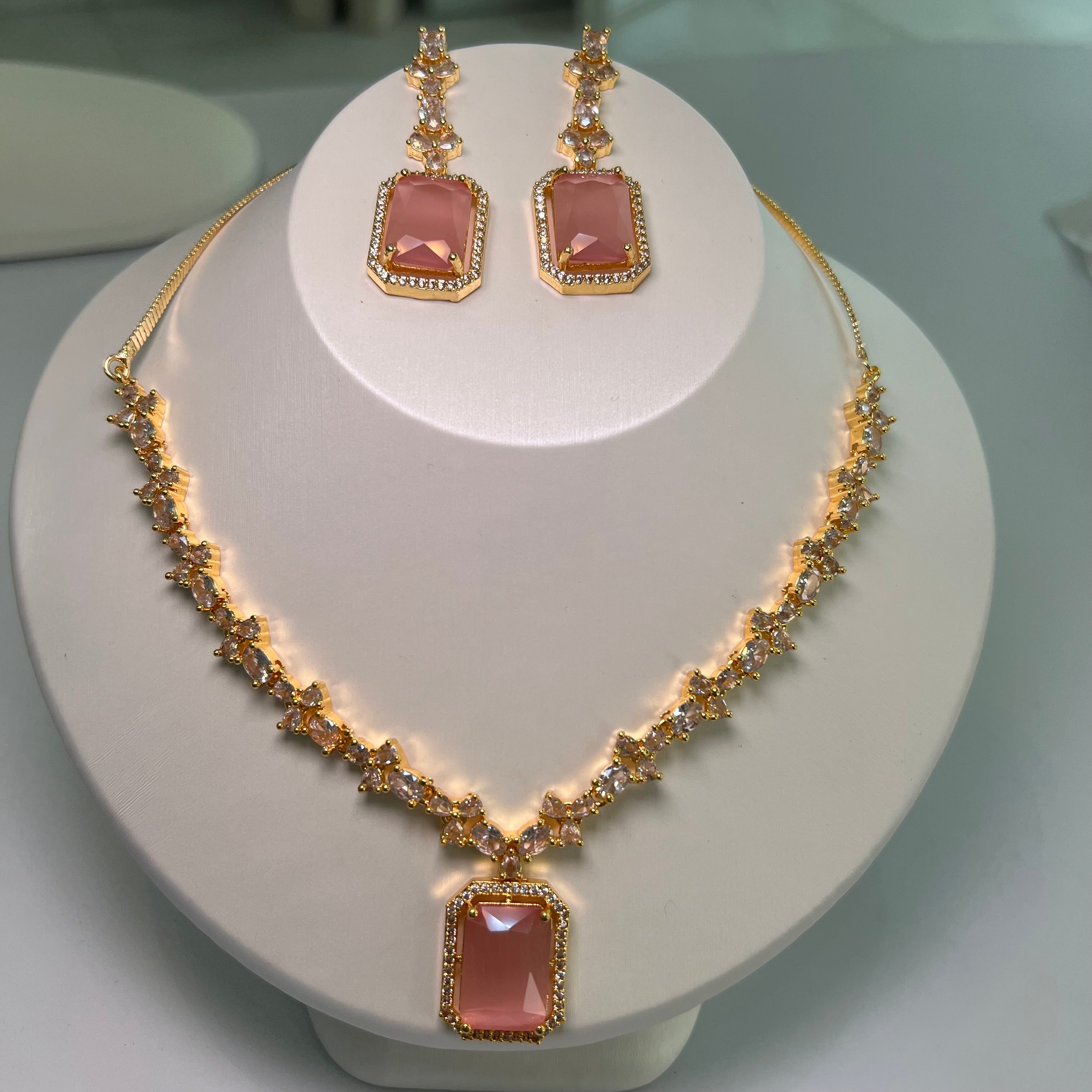 A gold-tone crystal charm necklace and earrings set with a rectangular centerpiece and drop earrings on a mannequin.