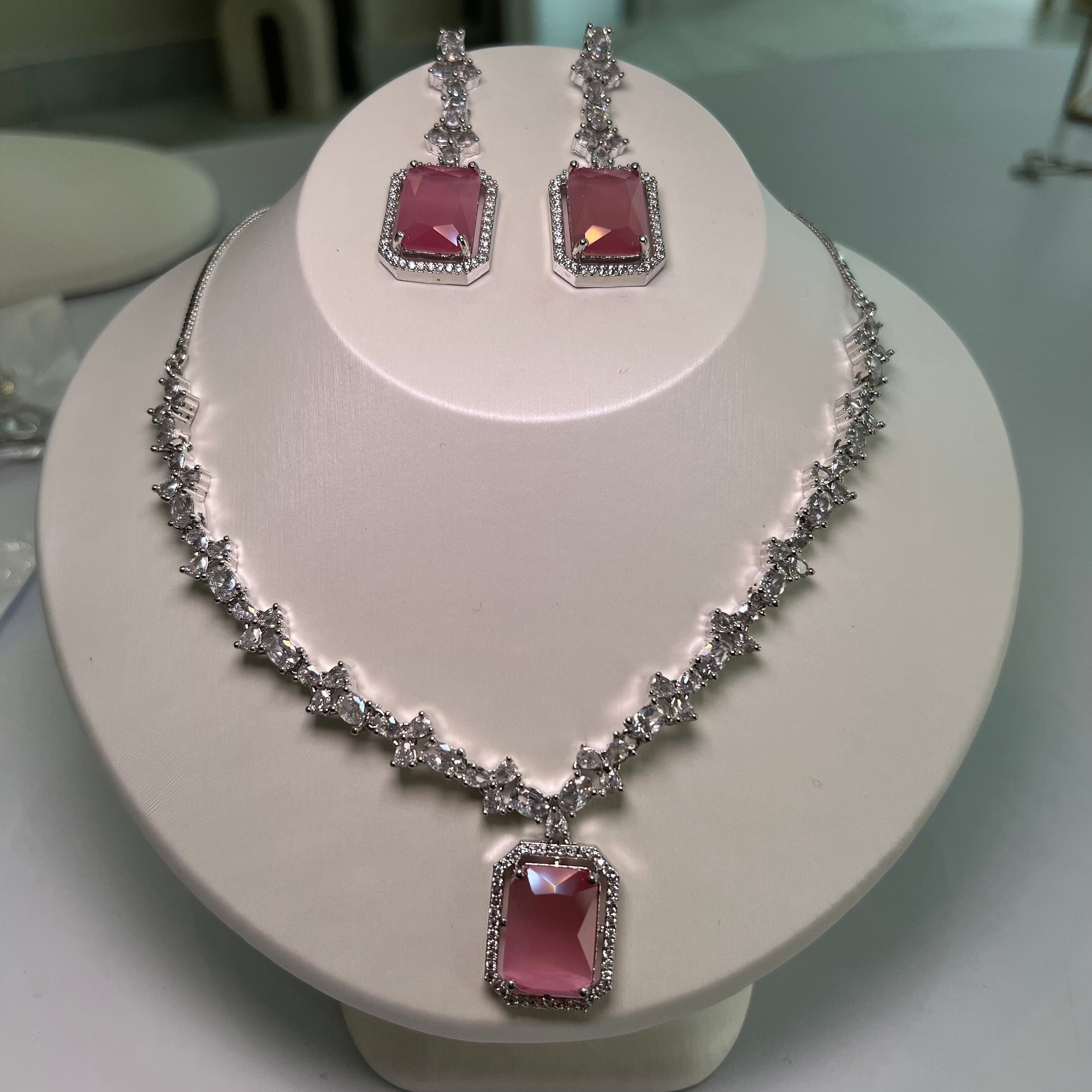 A silver-tone crystal charm necklace and earrings set with a rectangular centerpiece and drop earrings on a mannequin.