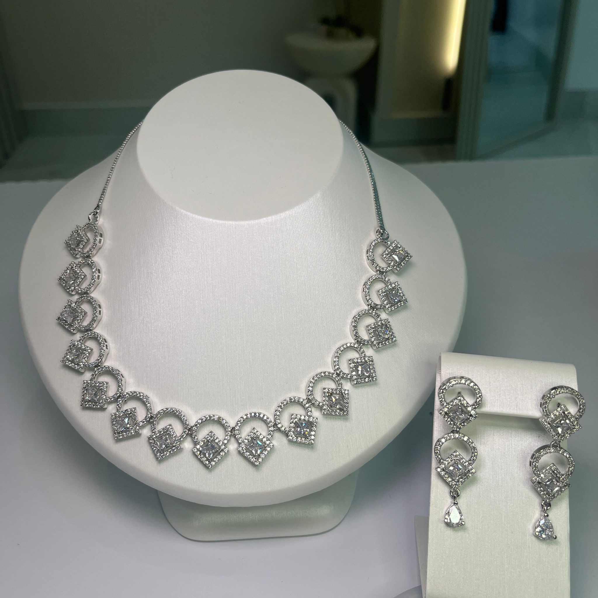 A jewelry set showcasing a wave-like necklace and matching earrings, adorned with clear crystals, displayed on a white mannequin bust.