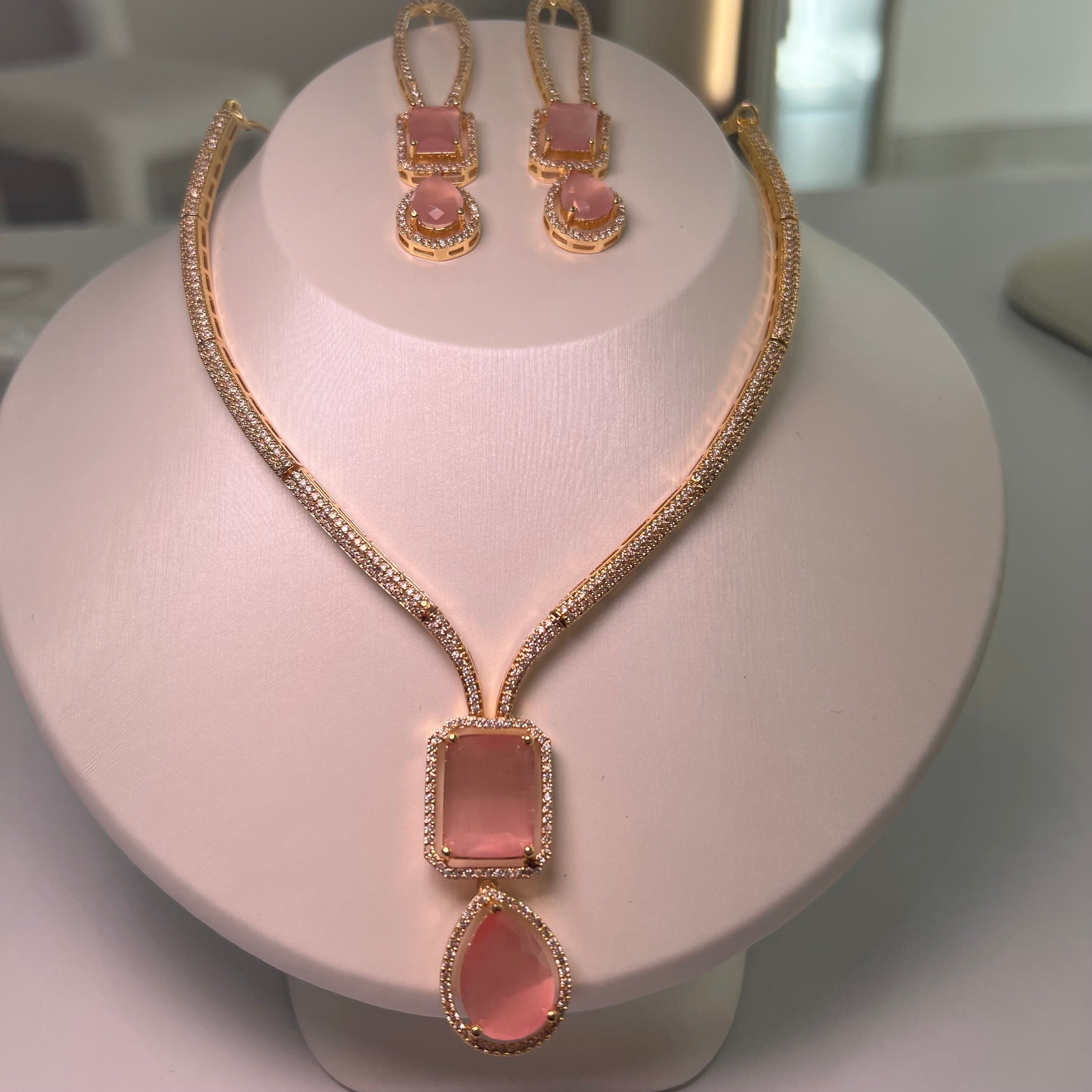 A gold-tone Empire Drape Necklace and Earrings set with pink gemstone pendants displayed on a mannequin bust