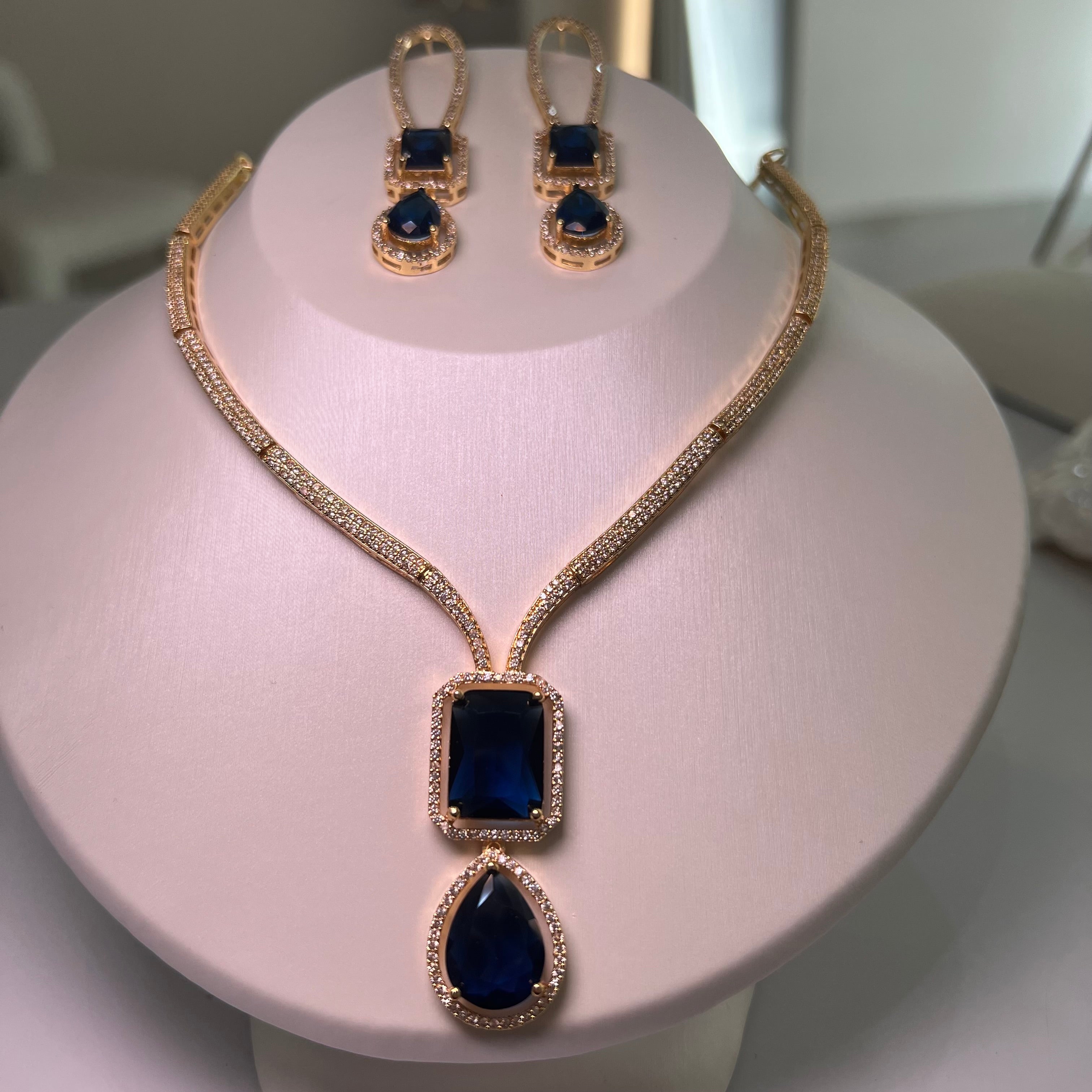 A gold-tone Empire Drape Necklace and Earrings set with dark-blue gemstone pendants displayed on a mannequin bust