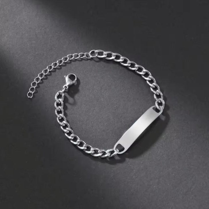 A silver-colored stainless steel bracelet with a curb chain design and an engraved bar pendant in the center.