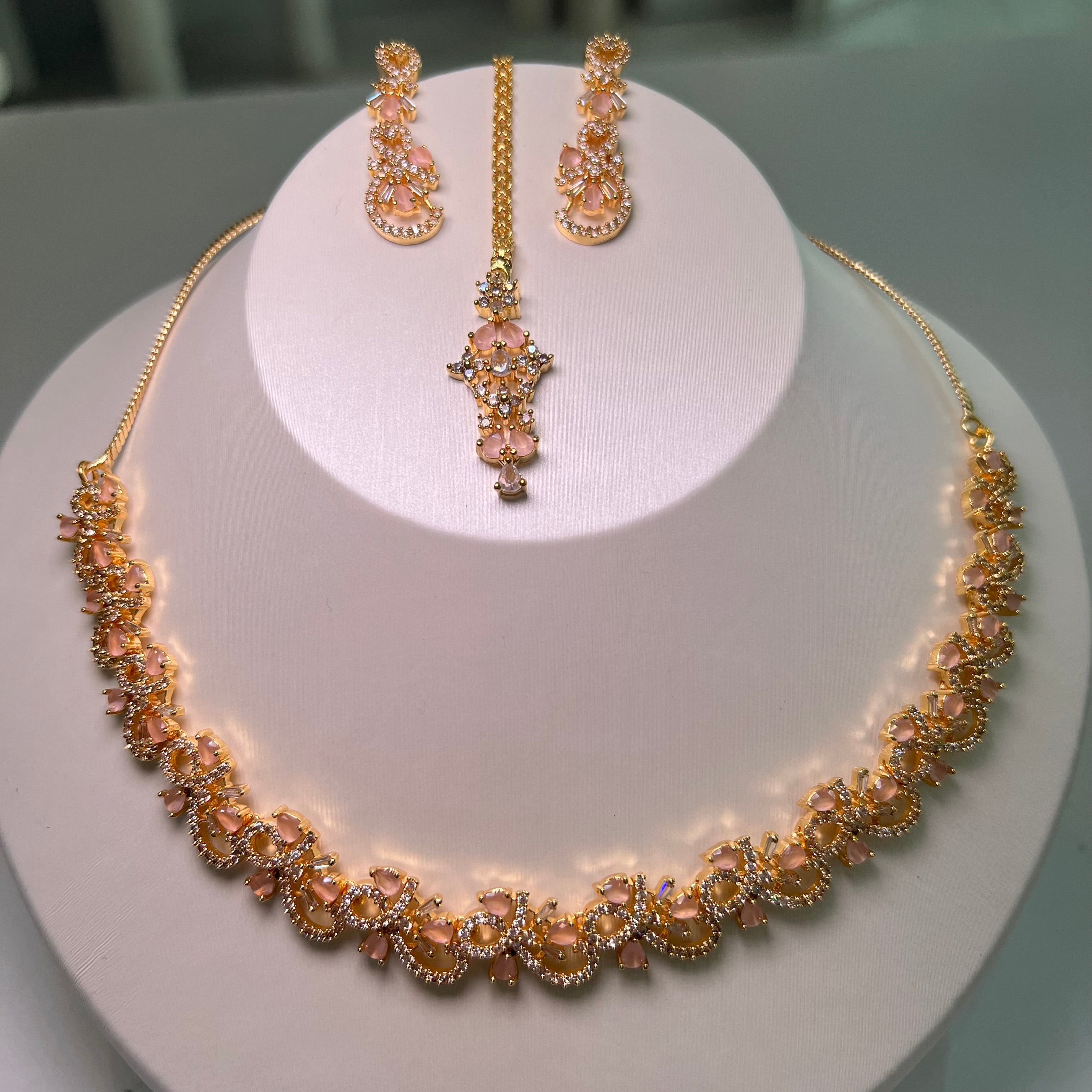 A necklace and earrings set displayed on a mannequin, featuring gold-tone chains with floral-inspired patterns and multicolored stones.