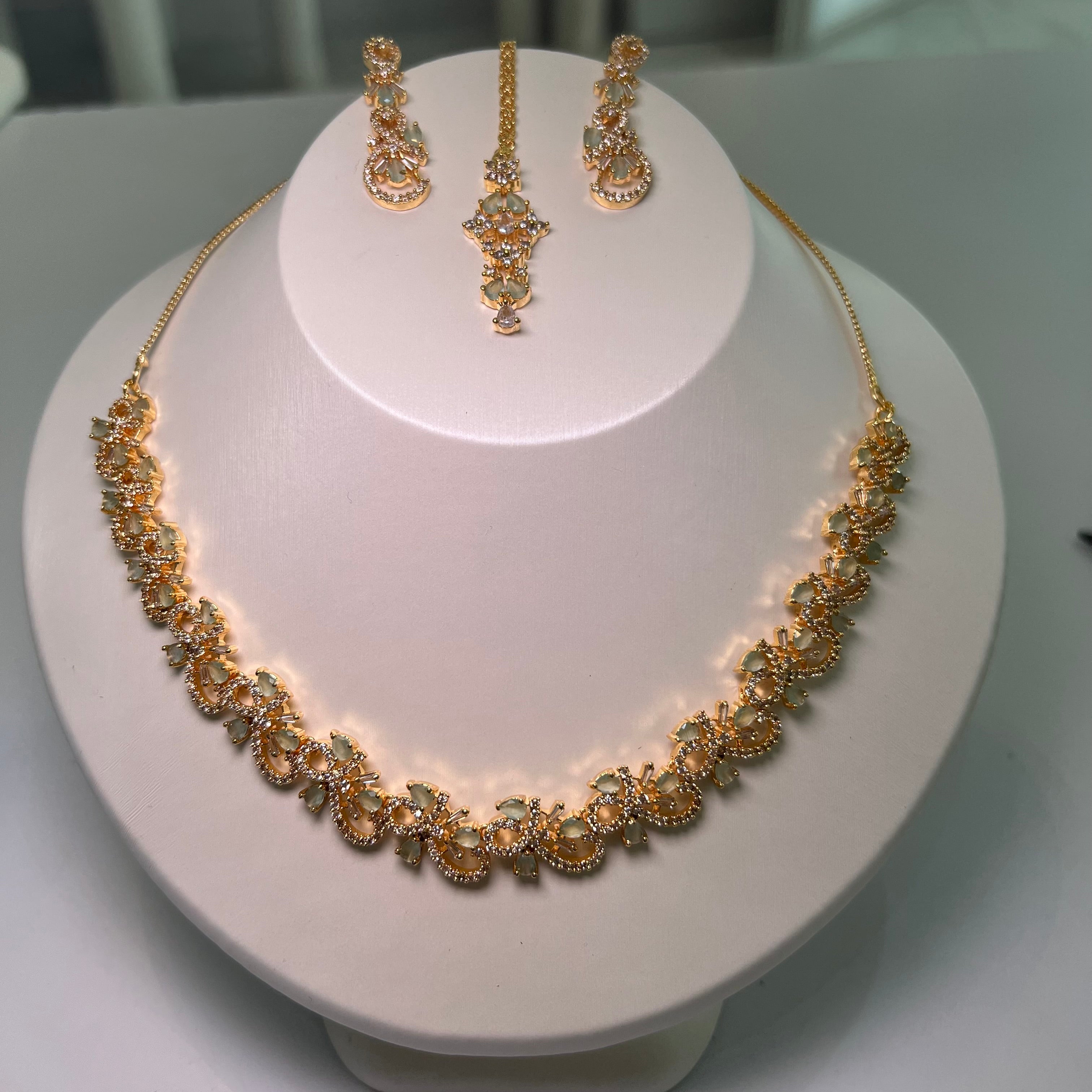 A necklace and earrings set displayed on a mannequin, featuring gold-tone chains with floral-inspired patterns and multicolored stones.