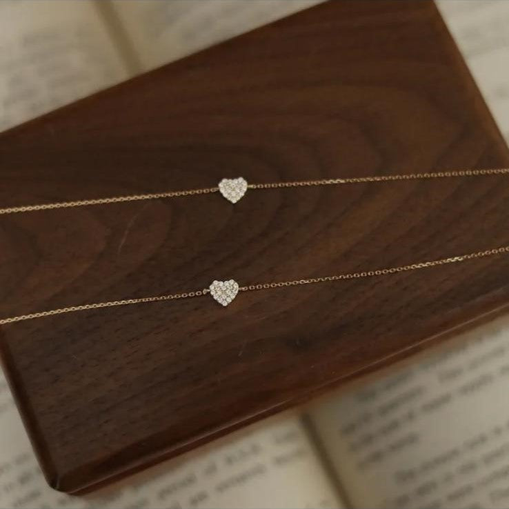 Two sterling silver bracelets with a gold plated zirconia heart design, displayed on a wooden block.