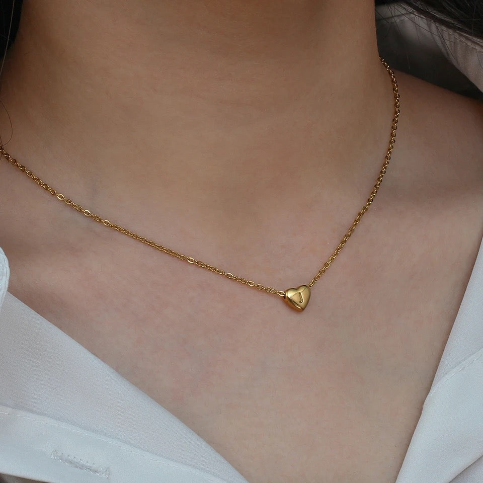 A gold-colored heart initial necklace with a letter on a chain.