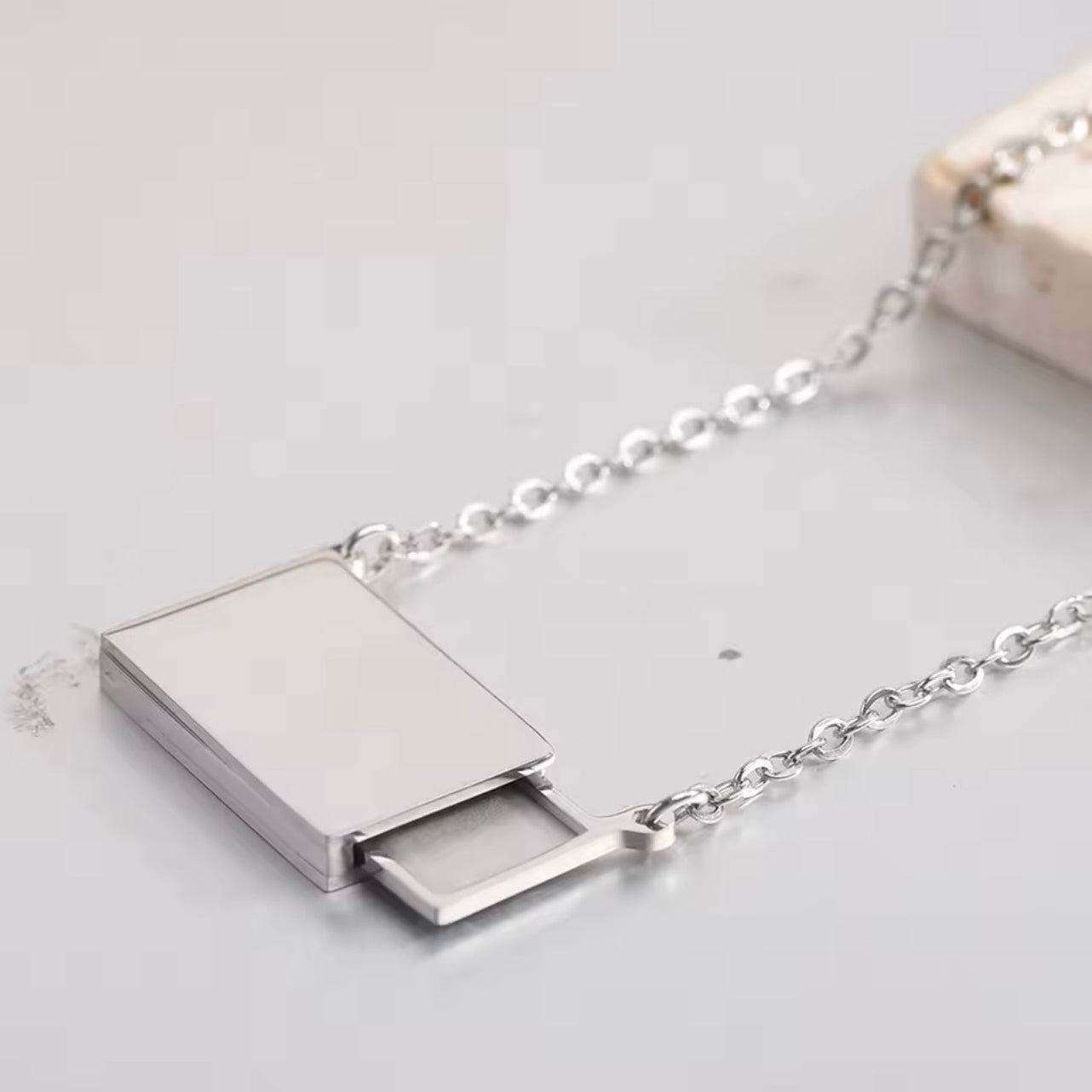 Silver necklace with a rectangular pendant on a light gray background