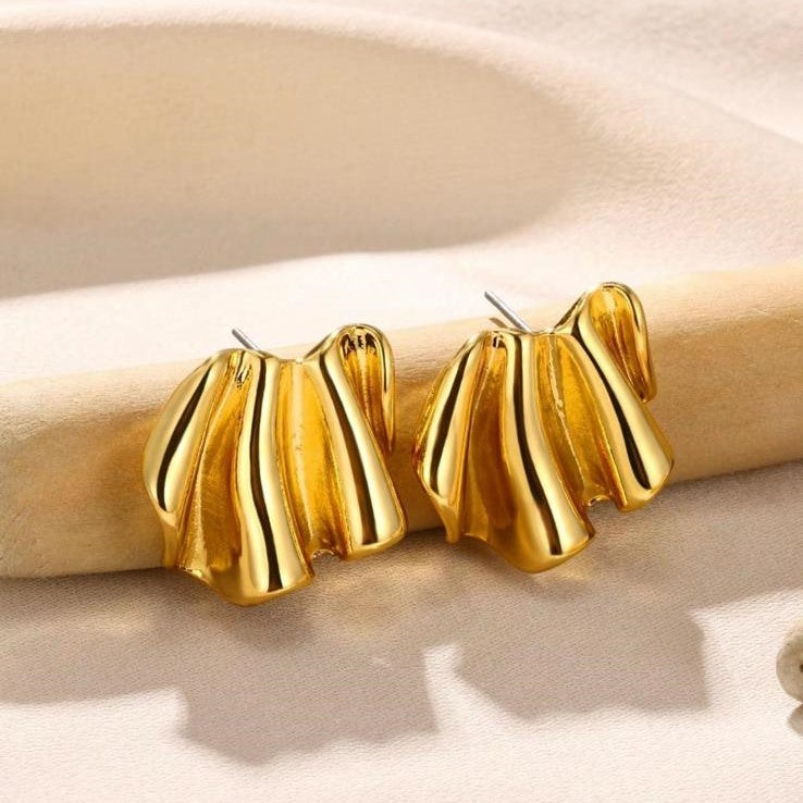 A pair of gold-colored, wave-shaped metal earrings resting on a beige surface.