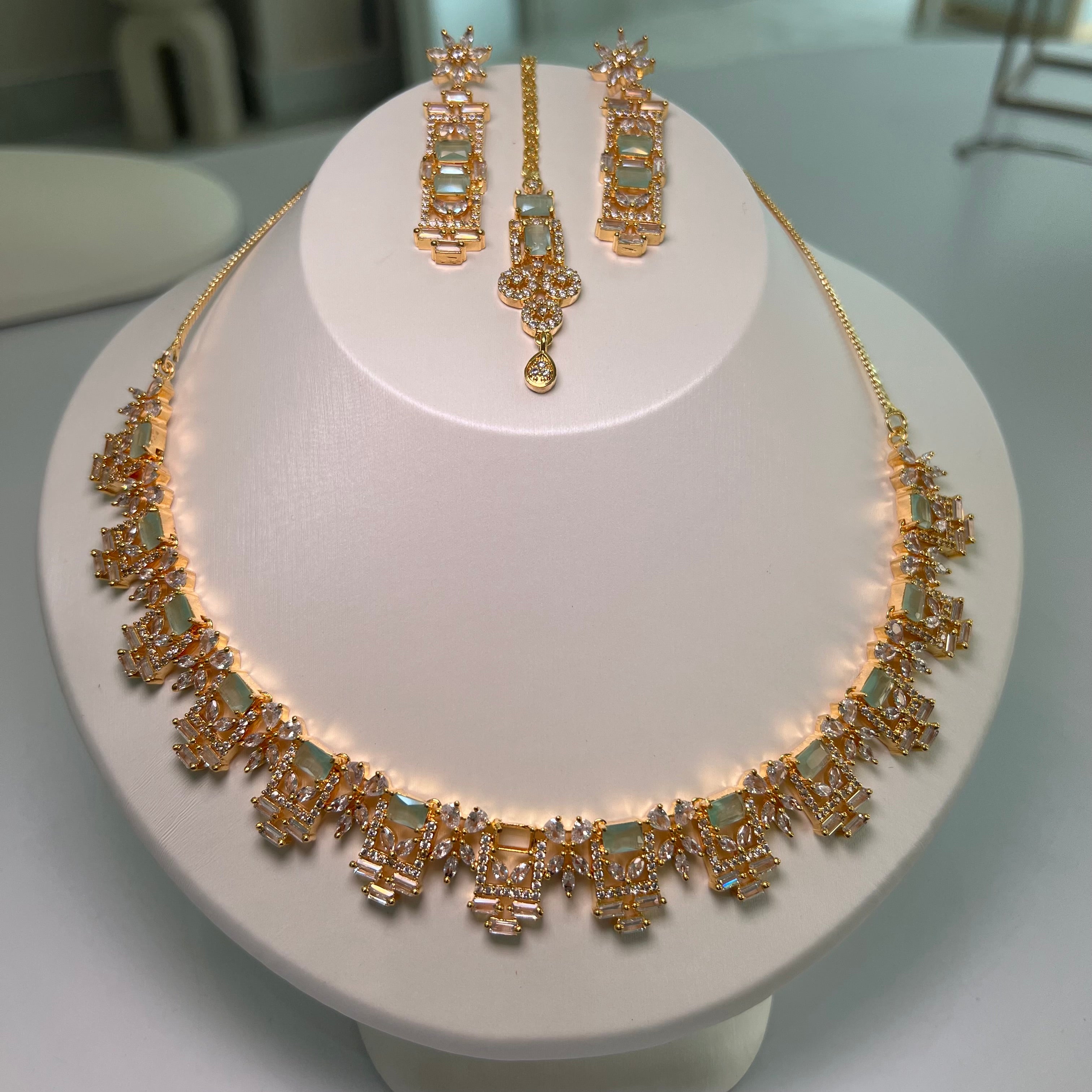 A gold-tone rectangle motif necklace with matching earrings displayed on a mannequin bust.