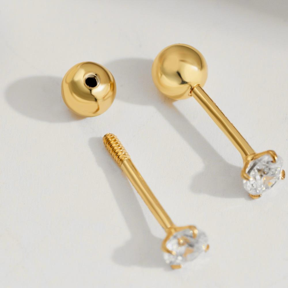 A pair of gold-plated barbell stud earrings with one stud earring featuring a clear, faceted gemstone on the end.