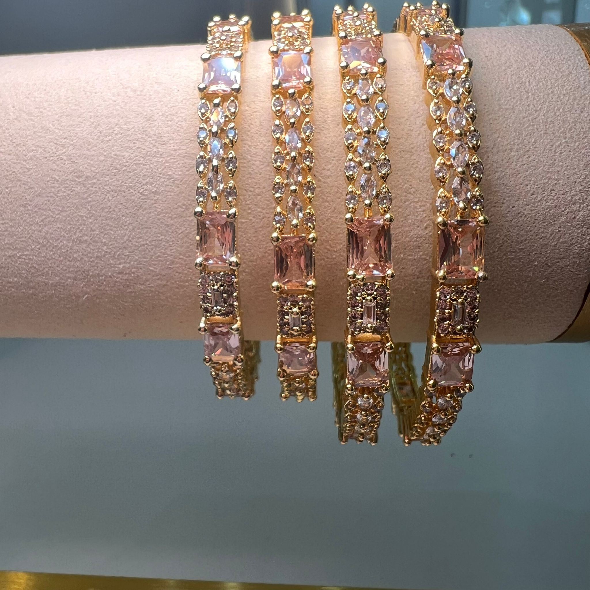 Gold bracelets with pink gemstones on a mannequin arm against a neutral background