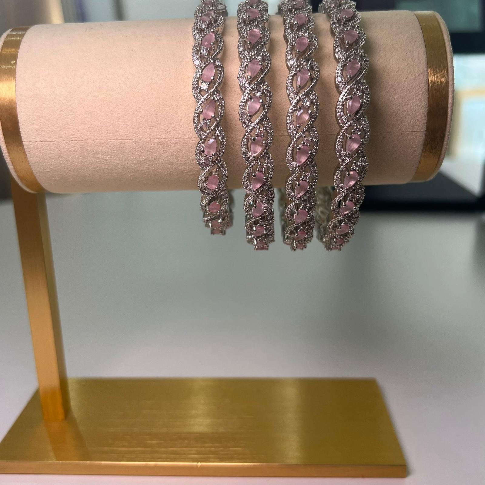 Four pink gemstone bracelets on a gold stand against a neutral background.