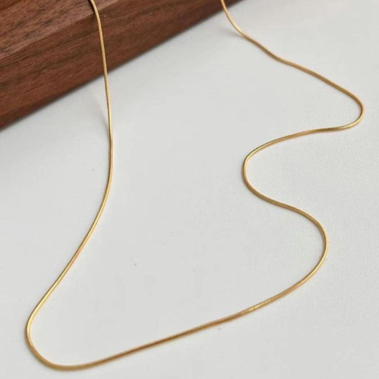 A sleek gold-colored stainless steel chain necklace displayed on a wooden surface.