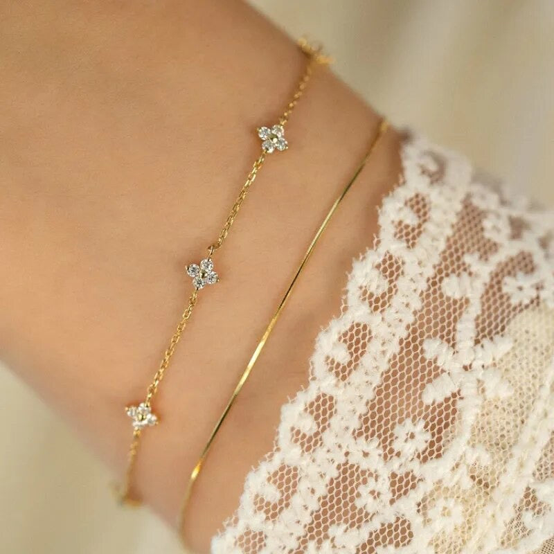 A small dainty flower bracelet with chain in gold color, featuring multiple small flowers as charms on the bracelet.