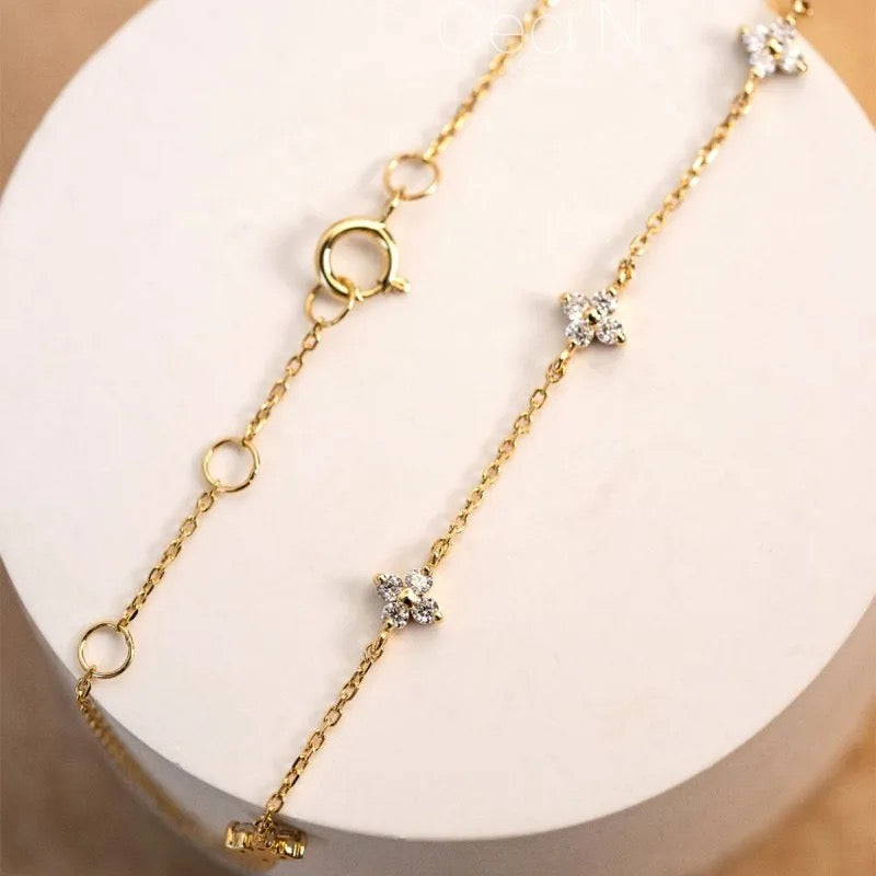 A small dainty flower bracelet with chain in gold color, featuring multiple small flowers as charms on the bracelet.