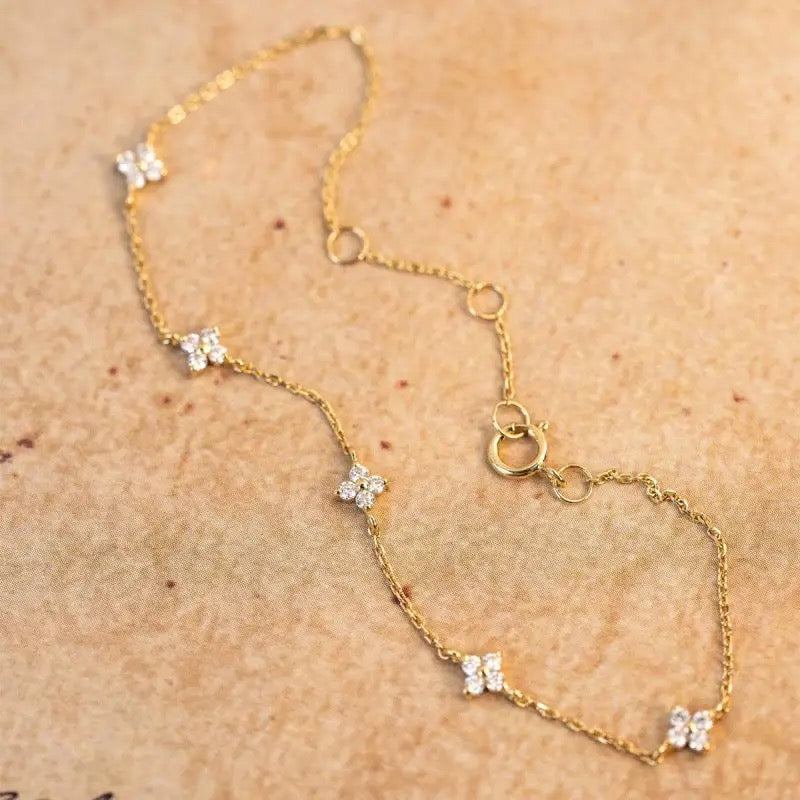 A small dainty flower bracelet with chain in gold color, featuring multiple small flowers as charms on the bracelet.