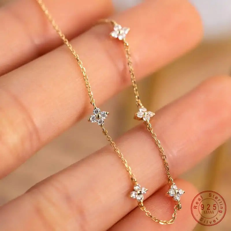 A small dainty flower bracelet with chain in gold color, featuring multiple small flowers as charms on the bracelet.
