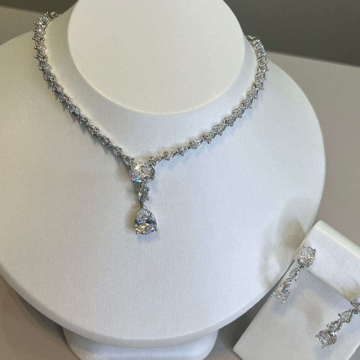 A teardrop necklace and earrings set displayed on a white mannequin. The set features a silver-tone chain with crystal embellishments and a teardrop pendant.