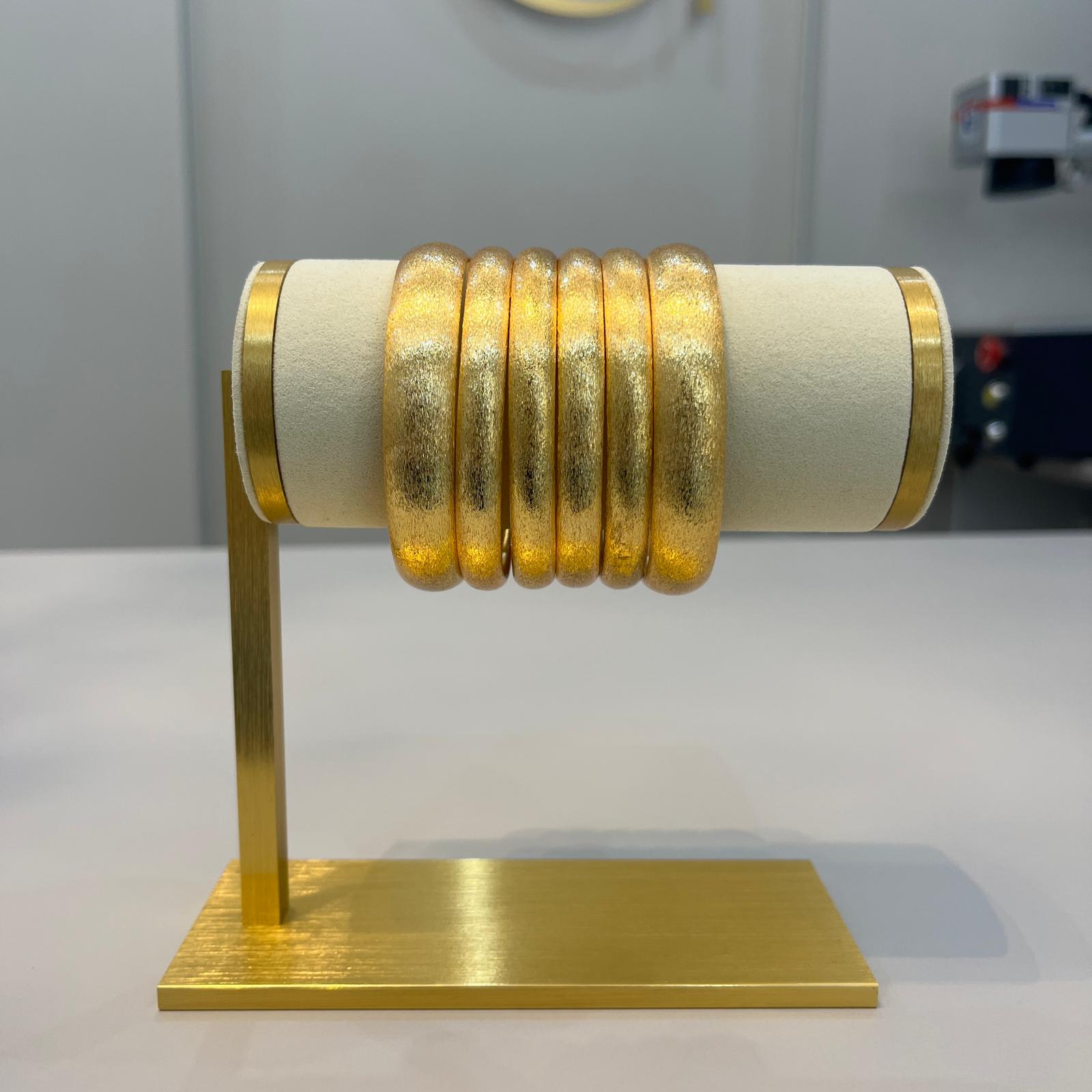 A set of six textured gold bangles displayed on a cylindrical stand.